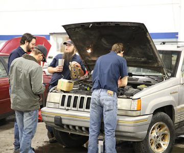 image of students working on a car in the auto shop