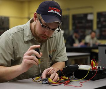 image of electrician student with screwdriver in hand working on an open piece of technology