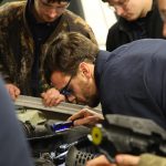 image of man bent over fixing car engine in shop