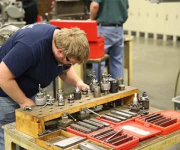 image of student standing over various pieces of equipment for the CNC machine.