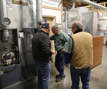 image of three men standing around a heating unit, going over the processes to fix it.