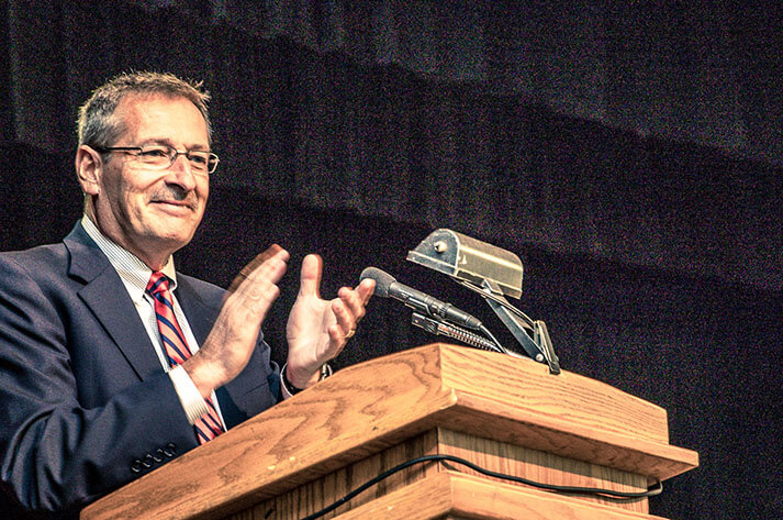 rex spaulding clapping as he stands at a podium at new castle school of trades graduation