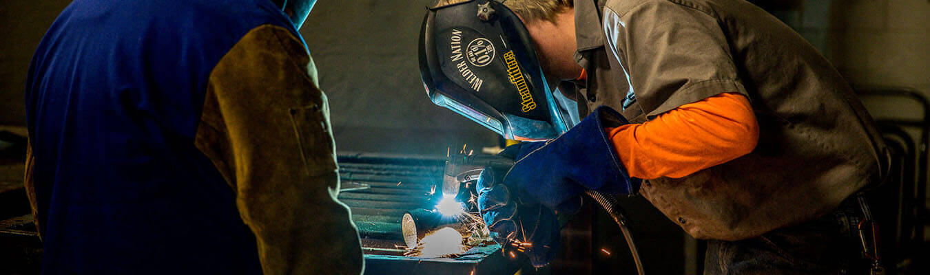 two NCST students with welding helmets on welding metal