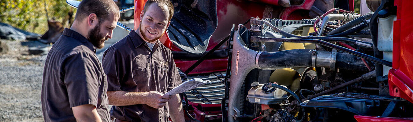 image of two students looking at the engine of a semi with the hood lifted