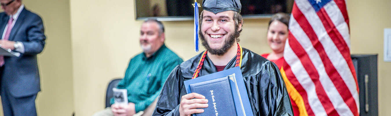 Image of NCST graduate wearing cap and gown, holding diploma