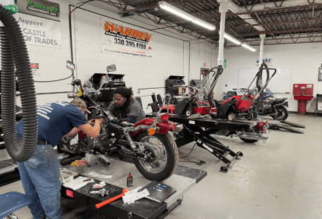 Image of two students working on a red motorcycle in a repair shop.