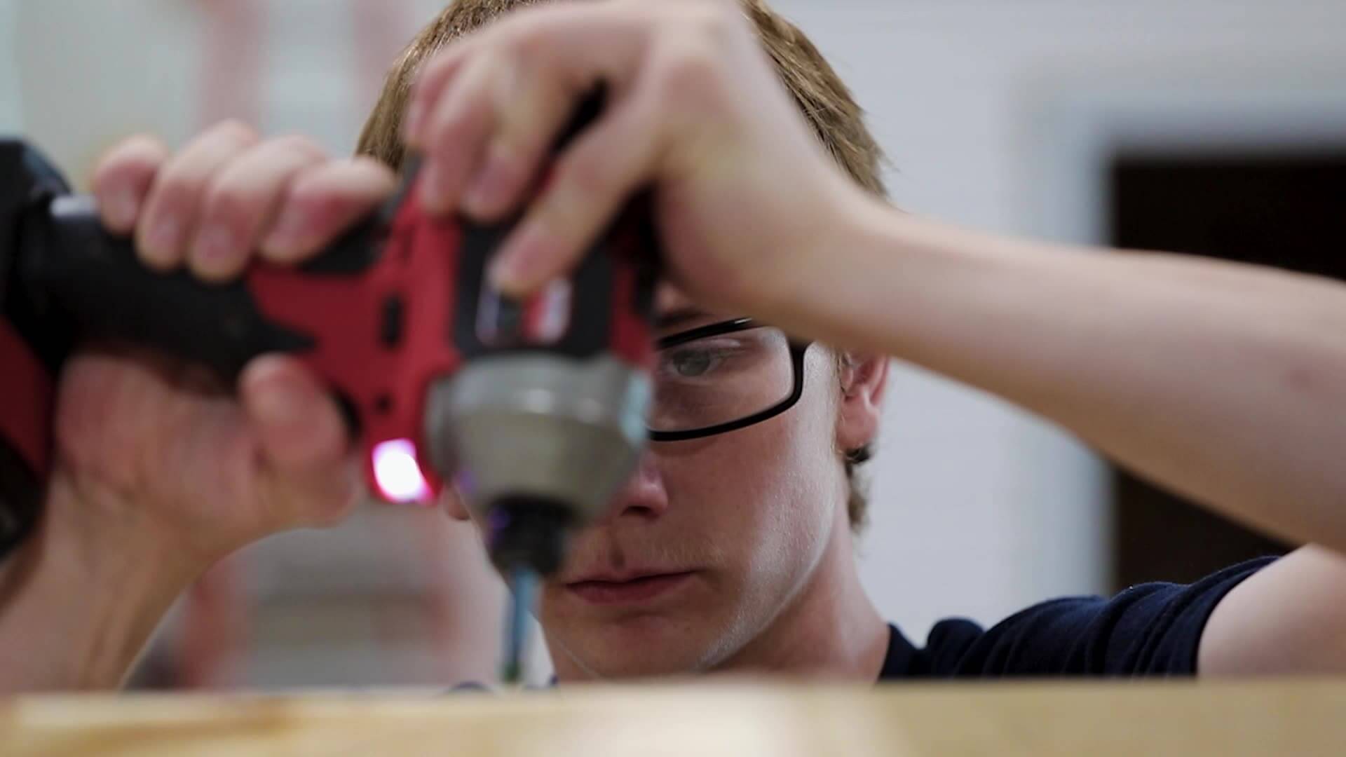 Closeup of Bryce using an electric screwdriver on a wood board