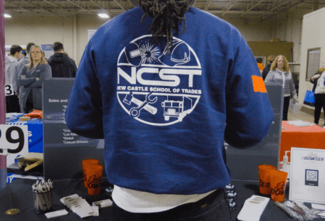 NCST student standing at career fair table, NCST emblem on back of his jacket