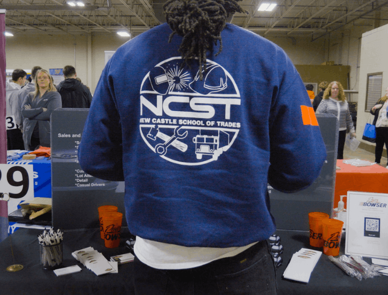 NCST student standing at career fair table, NCST emblem on back of his jacket