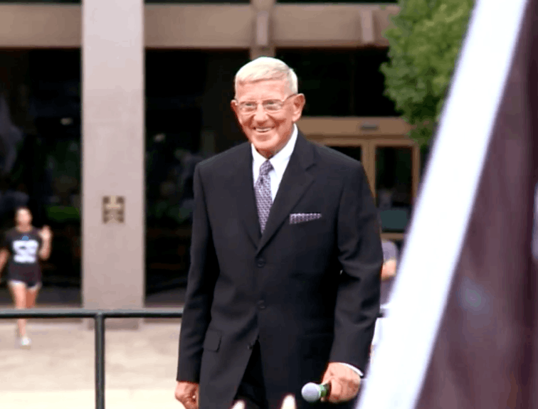 Lou holtz talking towards camera in front of building