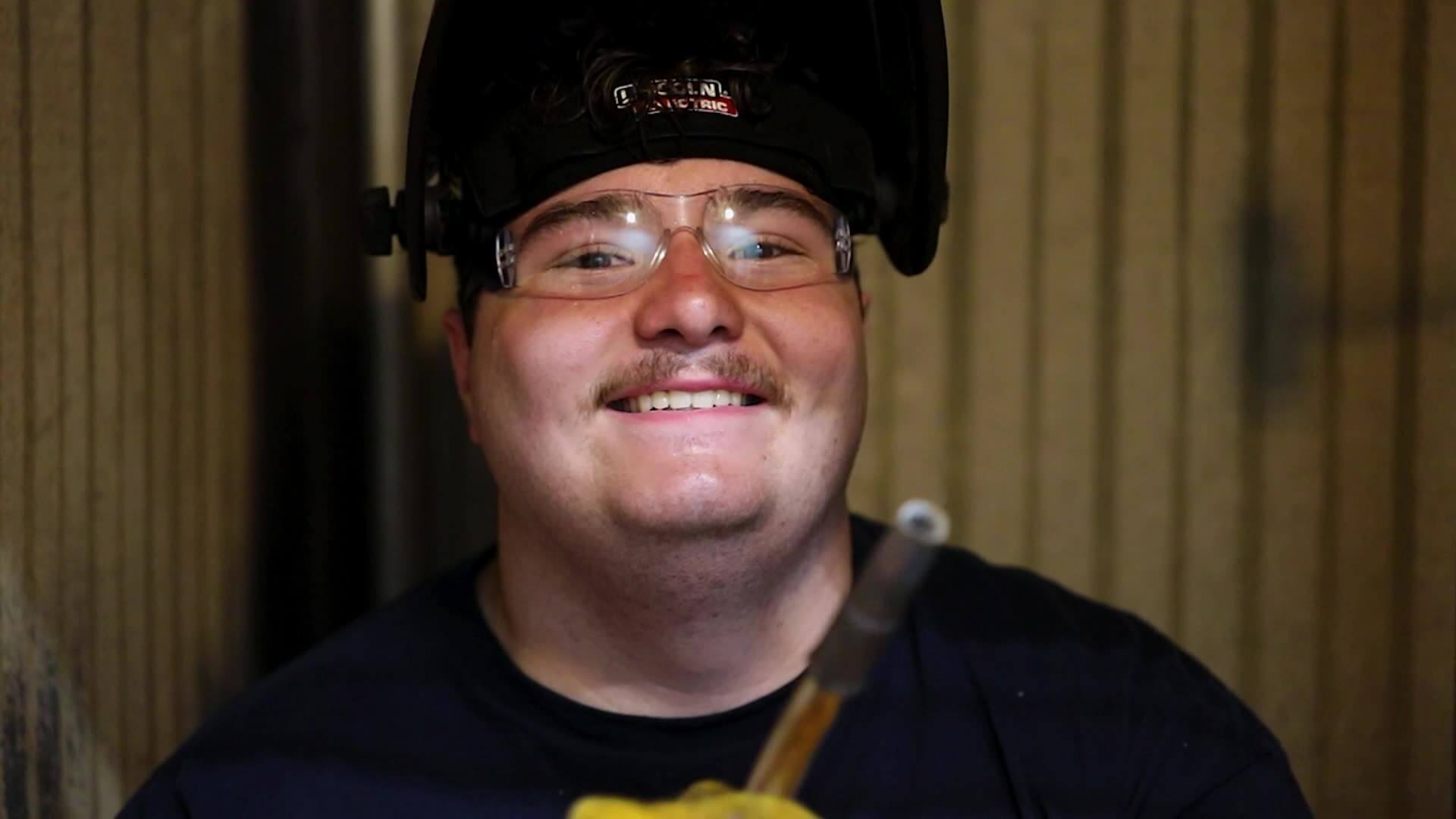 Closeup of Alex smiling while holding welding torch and welding mask on his head
