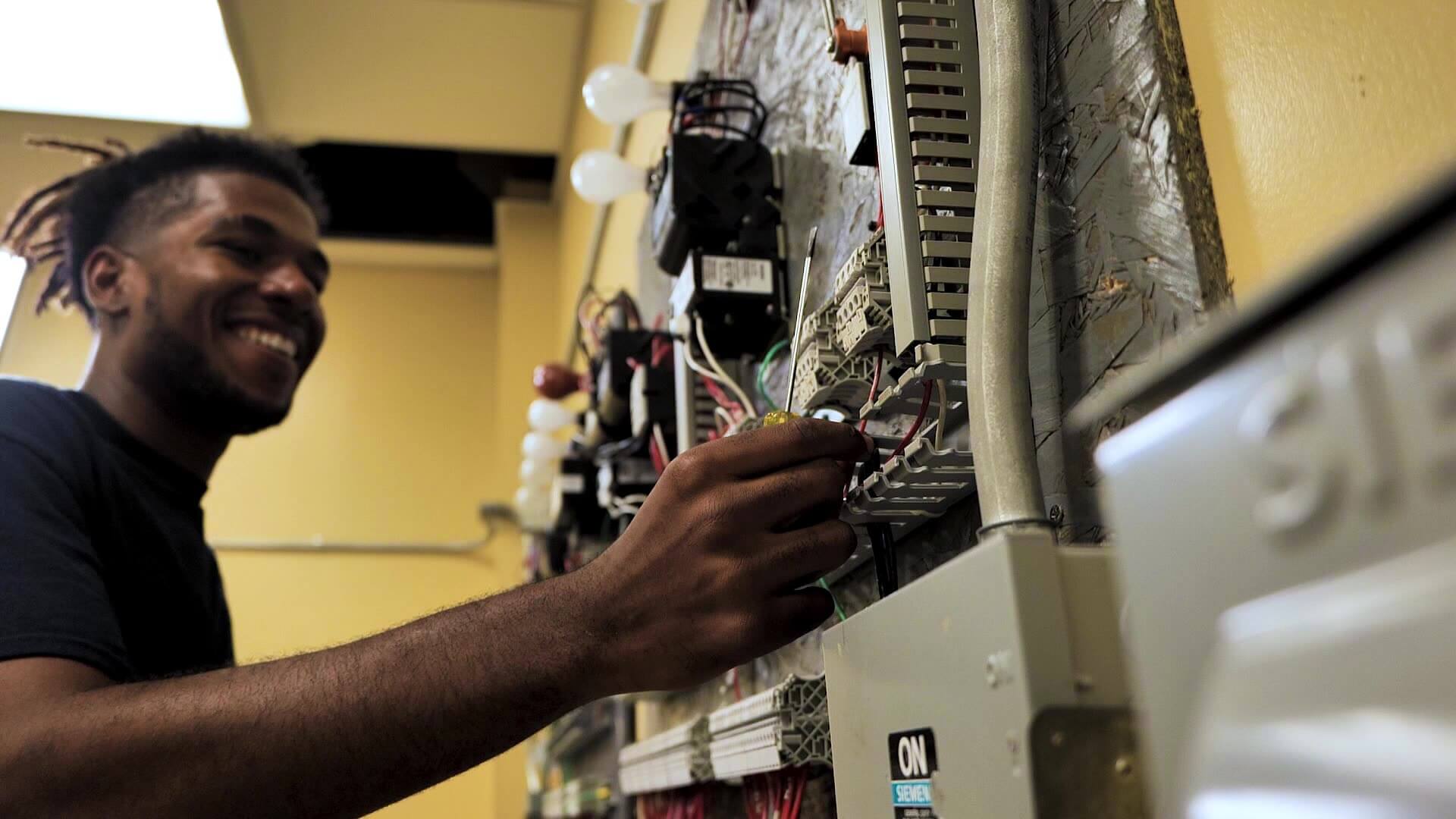 Closeup of Kenneth smiling and working on electric circuit panels