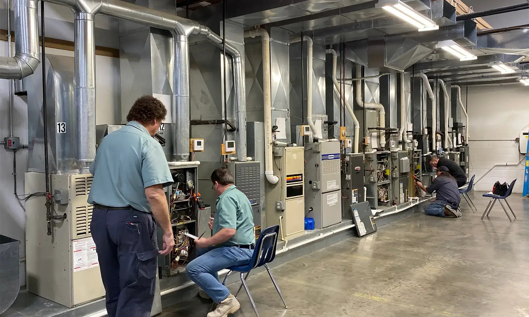 HVAC trade school students working on a row of residential furnace and air handler units in a hands-on heating and cooling training lab