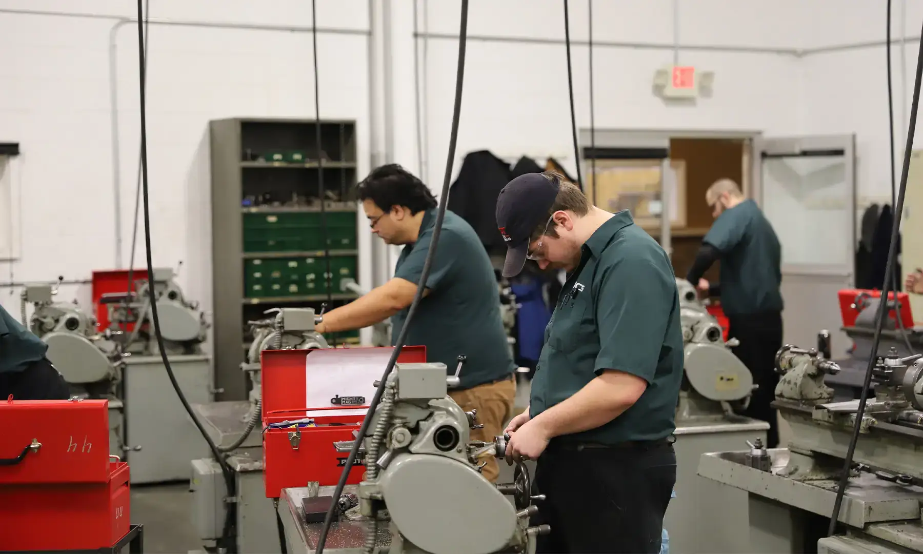 Machinist and CNC manufacturing trade school students in uniform work independently on manual lathes in a large machine shop training lab